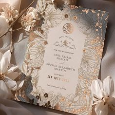 the wedding card is surrounded by flowers and satin material, with gold foil on it