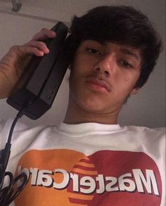 a young man holding a cell phone up to his ear while wearing a mastercard t - shirt