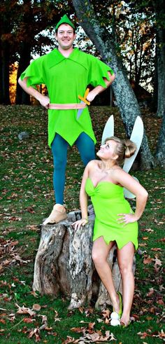 two people dressed as peter pan and tinkerbells sitting on a tree stump