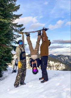 two people standing on top of a snow covered slope holding up a snowboard above their head