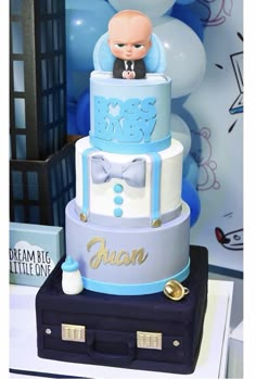 a three tiered cake with a baby on top and blue balloons in the background