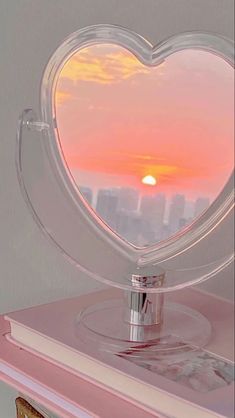 a heart shaped mirror sitting on top of a pink table next to a book case