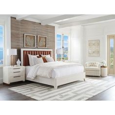 a bedroom with a bed, dresser and chair next to two windows overlooking the ocean