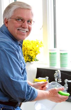 a man standing in front of a sink holding a green toothbrush and soap bottle