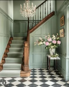 a room with stairs, chandelier and flowers in vases on the floor