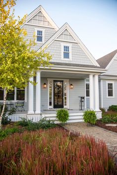 a gray house with white trim on the front door and windows, along with landscaping