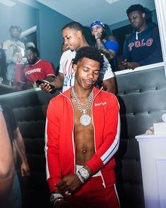 young man in red sweat suit looking at his cell phone while other people look on