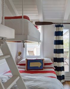 a bedroom with bunk beds, striped curtains and a ladder to the ceiling in front of a window