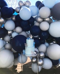 a blue and white cake sitting on top of a table next to balloons in the shape of snowflakes