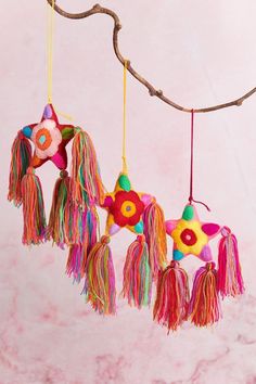 three colorful tassels hanging from a branch on a pink marble background with a tree branch in the foreground