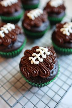 chocolate cupcakes decorated with white frosting and football decorations on a cooling rack