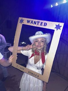 a woman in a white dress and cowboy hat holding up a cardboard sign that says wanted