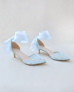 a pair of blue high heeled shoes with a white bow on the toe and lace detailing