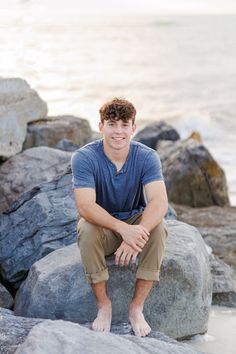 a young man is sitting on some rocks by the water