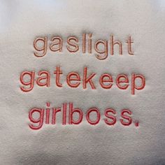 the words are embroidered onto white material with red thread on it, which reads gaslight gatekeeper girlboss