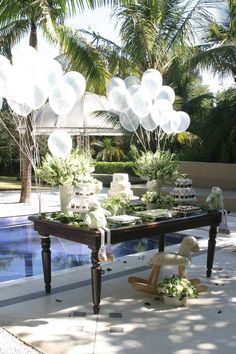 an outdoor party with balloons and flowers on the table by the pool is ready to be served