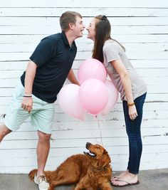 a man and woman standing next to a brown dog with pink balloons in front of them