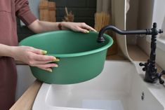 a woman is holding a green bowl over a white sink with black faucet