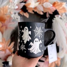 a hand holding a black coffee mug with ghost and stars on it