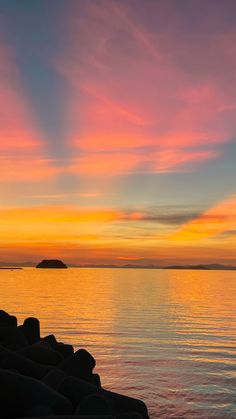 the sun is setting over the water and some rocks