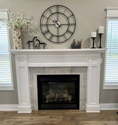 a fireplace with a clock on the mantle above it and two windows in the background