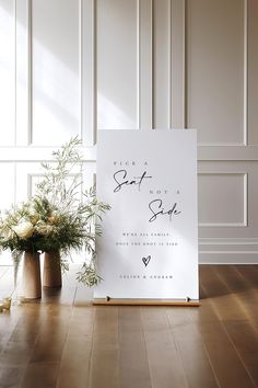 a sign sitting on top of a wooden floor next to two vases filled with flowers