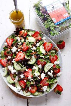 a salad with strawberries, cucumbers and feta cheese on it next to a container of dressing