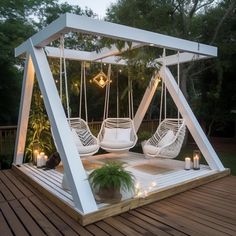 a porch swing with hanging chairs and candles on the deck in front of some trees