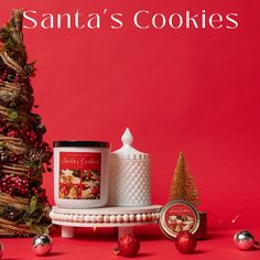 a red background with christmas decorations and cookies next to a white candle on a cake stand