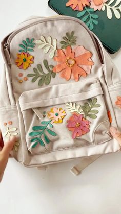 two purses with flowers painted on them and one is being held up by someone's hand