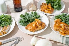 three white plates topped with food next to garlic and broccoli on a table