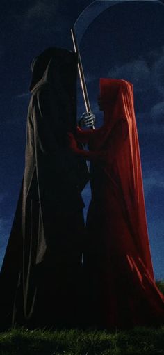 two people dressed in red and black standing next to each other on a hill at night