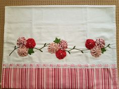 three red flowers on a white cloth with green leaves and pink striped border around the edges