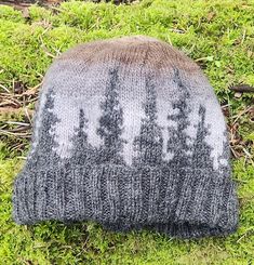 a knitted hat sitting on top of green grass covered in snowflakes and trees