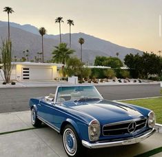 a blue car parked in front of a palm tree covered house with mountains in the background