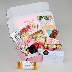 a pink box filled with lots of different types of food and candys next to a note