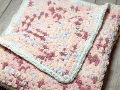 a pink and white crocheted blanket laying on top of a wooden floor next to a pair of scissors