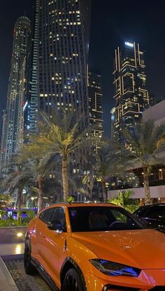 an orange suv is parked in front of some tall buildings at night with palm trees