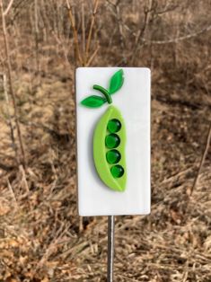 a green pea sitting on top of a white sign next to some grass and trees