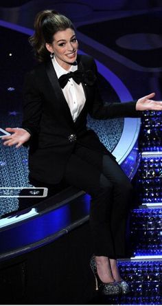 a woman in a tuxedo sitting on top of a table with her hands out