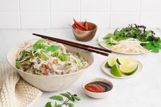 a bowl of food with chopsticks on the side next to bowls of vegetables and sauce