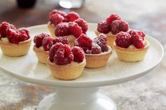 raspberry tarts are arranged on a white cake plate, ready to be eaten