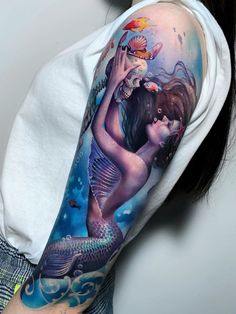 a woman with a mermaid tattoo on her arm holding a fish in front of her face