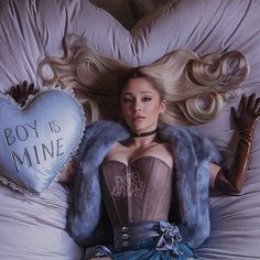 a woman laying on top of a bed wearing a corset and holding a heart shaped pillow