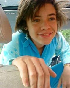 a young boy sitting in the back seat of a car with his hand on the steering wheel