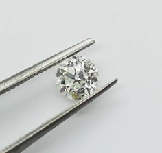 a diamond being cut by two tongs on a white surface with the tip still attached to it