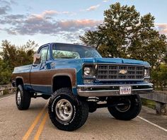 a blue truck parked on the side of a road next to a wooden fence with trees in the background