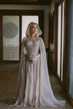 a woman in a wedding dress and veil standing on the floor with her hands behind her back