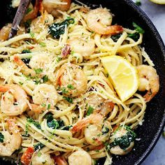 pasta with shrimp, spinach and parsley in a skillet next to lemon wedges