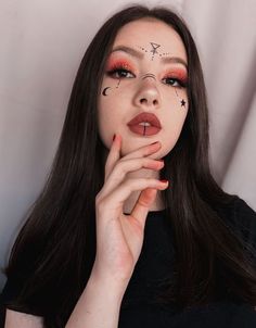 a woman with long black hair and red makeup is holding her hand up to her mouth